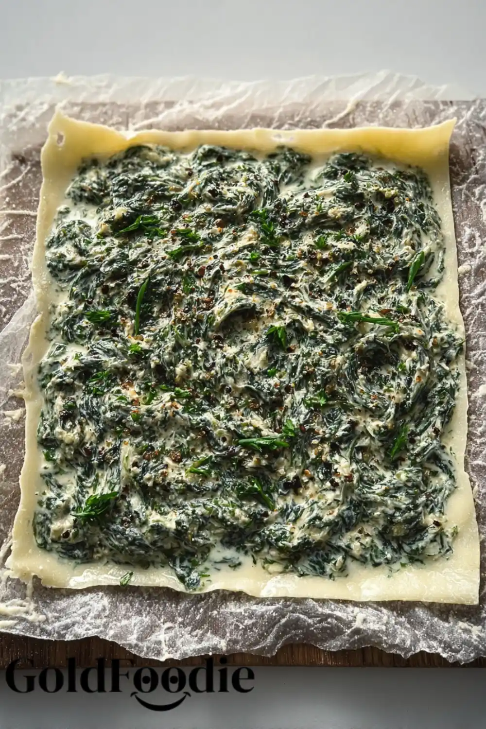 A raw sheet of puff pastry spread with an even layer of the spinach and ricotta filling, ready to be rolled