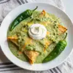 Authentic Hatch Chile Green Sauce Recipe 1 A bowl of homemade Hatch Chile green sauce surrounded by fresh green Hatch chiles and cilantro.