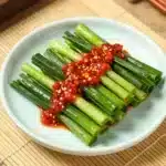 Garlic Chive Kimchi (Buchu Kimchi) Recipe 2 A close-up of Garlic Chive Kimchi (Buchu Kimchi) in a white bowl, showcasing vibrant green chives and red seasoning.