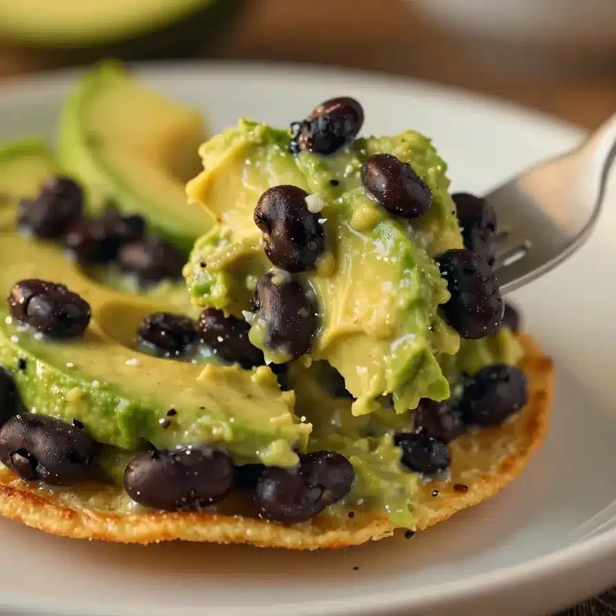 Creamy Black Bean Avocado Tostadas 5 A plate of creamy black bean avocado tostadas garnished with fresh cilantro and lime wedges.