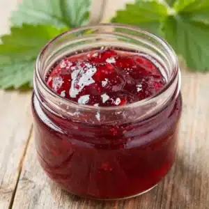 A jar of homemade rhubarb and strawberry jam on a wooden table.