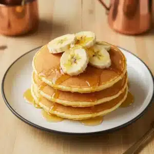 Fluffy banana pancakes stacked on a plate with fresh banana slices