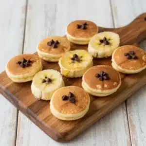 A stack of banana pancake pops served on a wooden plate with syrup drizzled on top