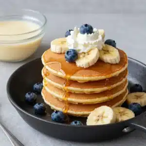 A stack of fluffy banana pancakes topped with sliced bananas and syrup