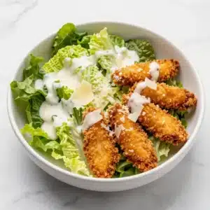 A vibrant Crispy Chicken Caesar Salad served in a bowl with croutons and parmesan cheese