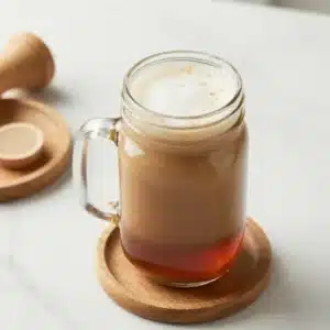 Homemade chai syrup in a glass jar next to a cup of chai latte on a wooden table.