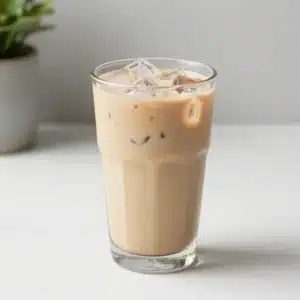 A light iced chai latte in a clear glass filled with ice and topped with a creamy cinnamon-spiced foam