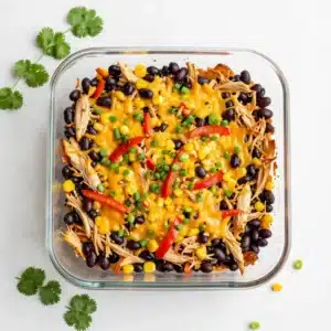 A baked chicken burrito casserole topped with melted cheese, salsa, and chopped cilantro in a casserole dish.