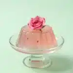 Rose Jello Cake 2 A rose jello cake with a glossy pink gelatin layer and decorative rose-shaped topping on a white serving plate.