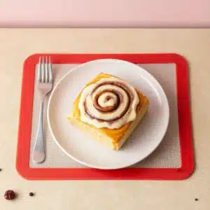Freshly baked pumpkin cinnamon rolls topped with creamy icing on a plate